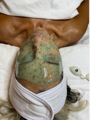 Person wearing a white garment with a greenish-brown pattern on a plain background